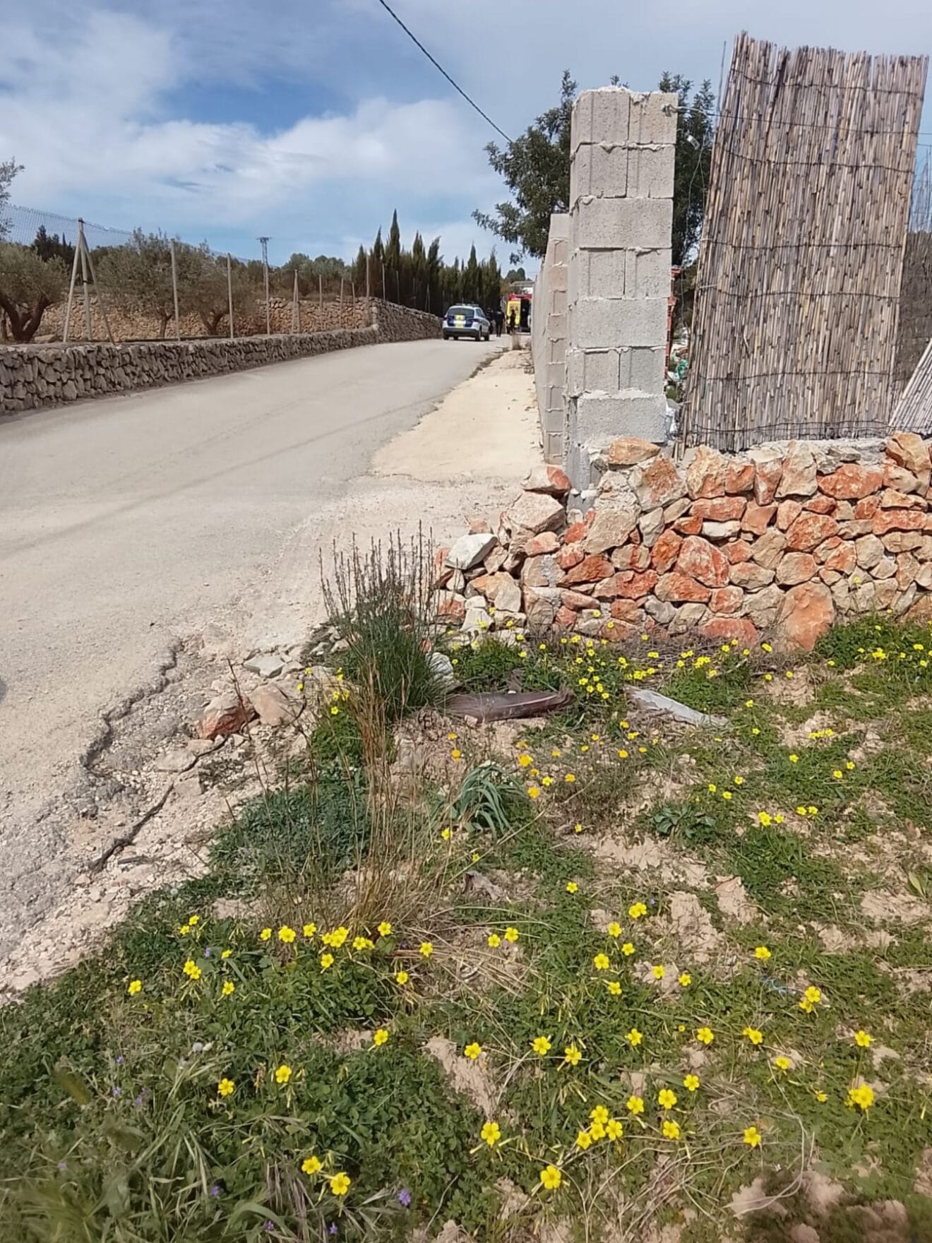 Camino rural en la partida Collado de Benissa, donde se produjo la caída del ciclista, con presencia de los servicios de emergencia al fondo