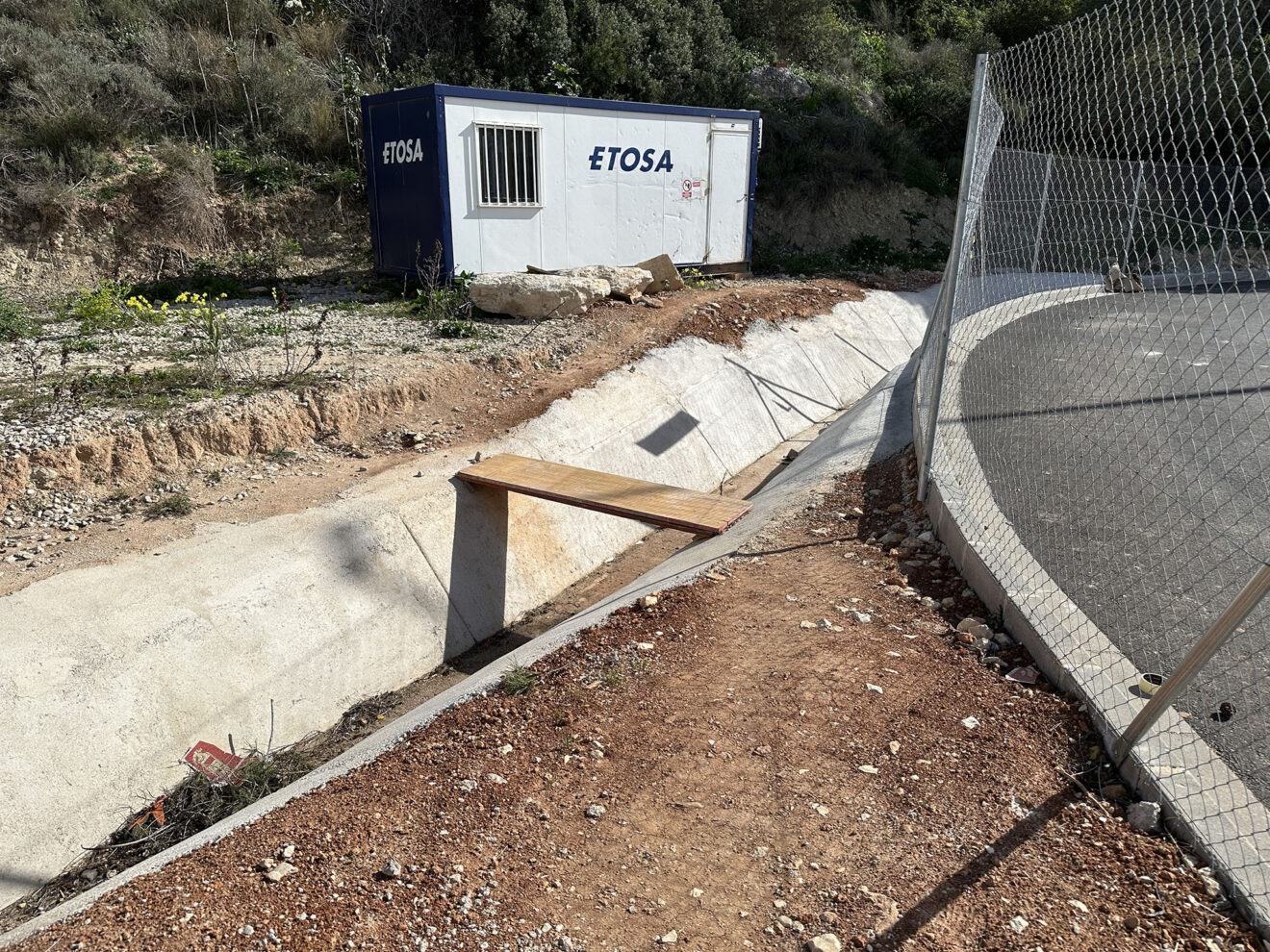 Lateral del parking sin vallar con acceso a una acequia y los contenedores de la empresa de las obras del CEIP Oltà e IES Les Salines de Calp
