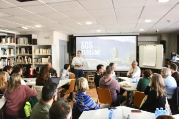 Sala de la biblioteca municipal con varios grupos de personas sentadas alrededor de mesas de trabajo
