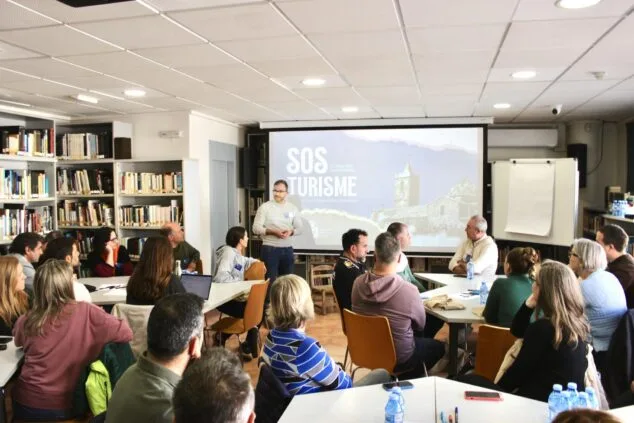 sala de la biblioteca municipal con varios grupos de personas sentadas alrededor de mesas de trabajo