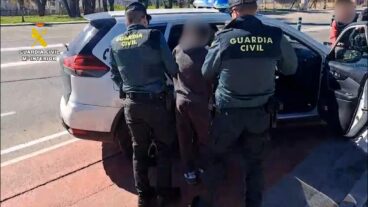 Dos agentes de la Guardia Civil detienen a una persona y la introducen en un coche patrulla.