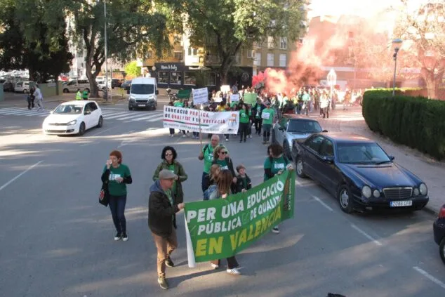 Manifestantes marchan con pancartas y humo rojo por la educación pública en una calle de Dénia.