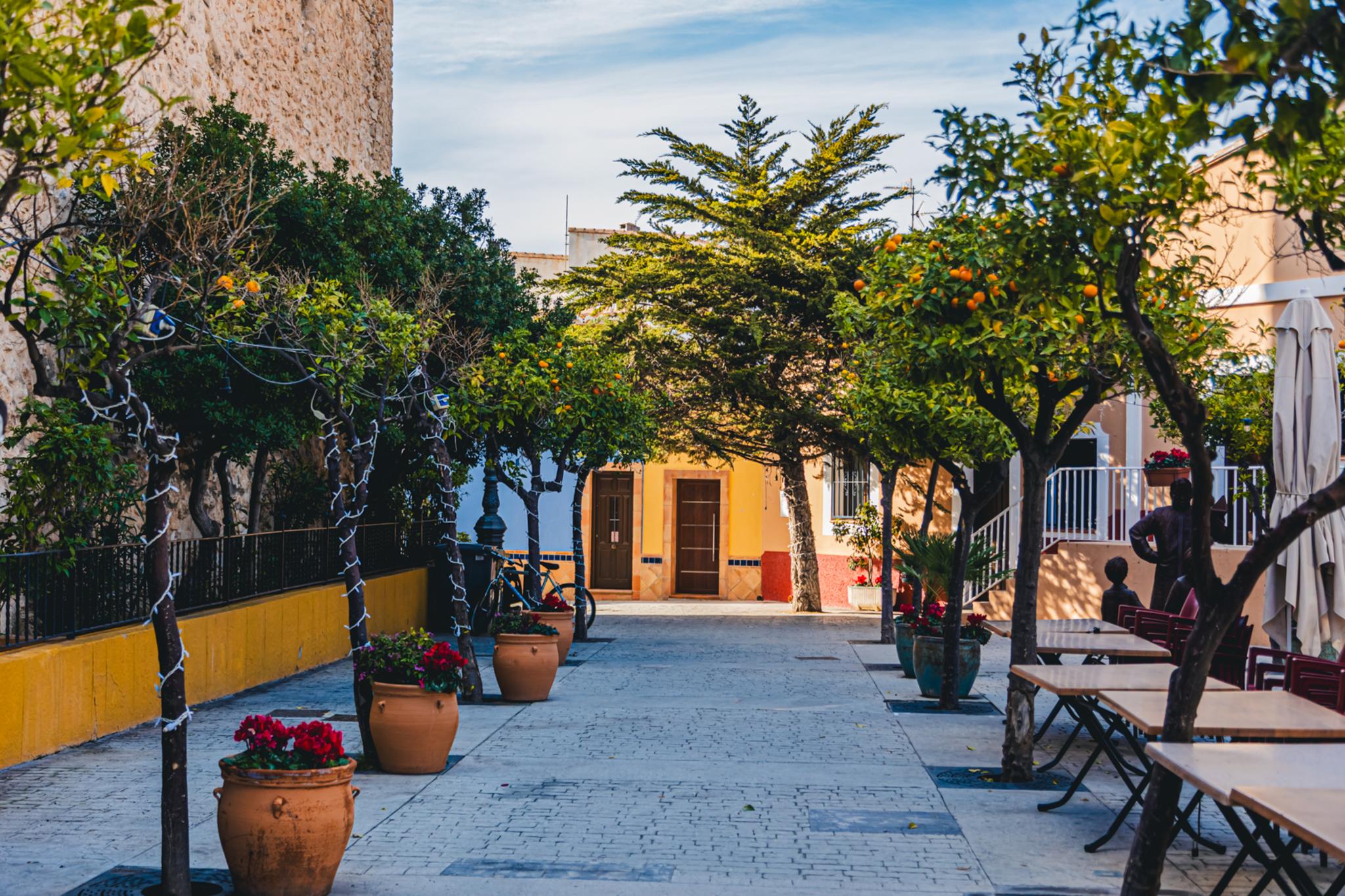 Pintoresca calle del casco antiguo de Calp con naranjos en macetas y mesas de terraza