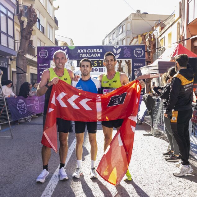 Imagen: Tres corredores masculinos ganadores posan con una bandera en la meta de la XXII Volta Popular Teulada.