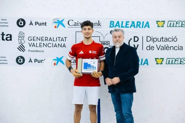 Eine Spielerin der valencianischen Pilota-Mannschaft Ondara hält die Meisterschaftstrophäe der CaixaBank Raspall Pro2 League neben einem Manager vor einem Gremium von Sponsoren in den Händen.