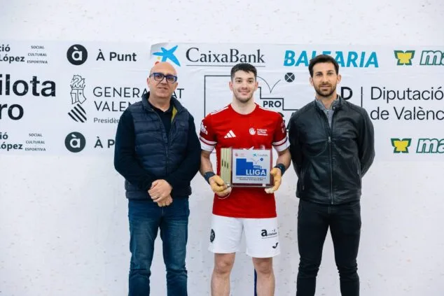 Ein Spieler des Teams Ondara hält die Meisterschaftstrophäe der CaixaBank Raspall Pro2 League in den Händen, begleitet von zwei institutionellen Vertretern vor einem Wettbewerbsbanner.
