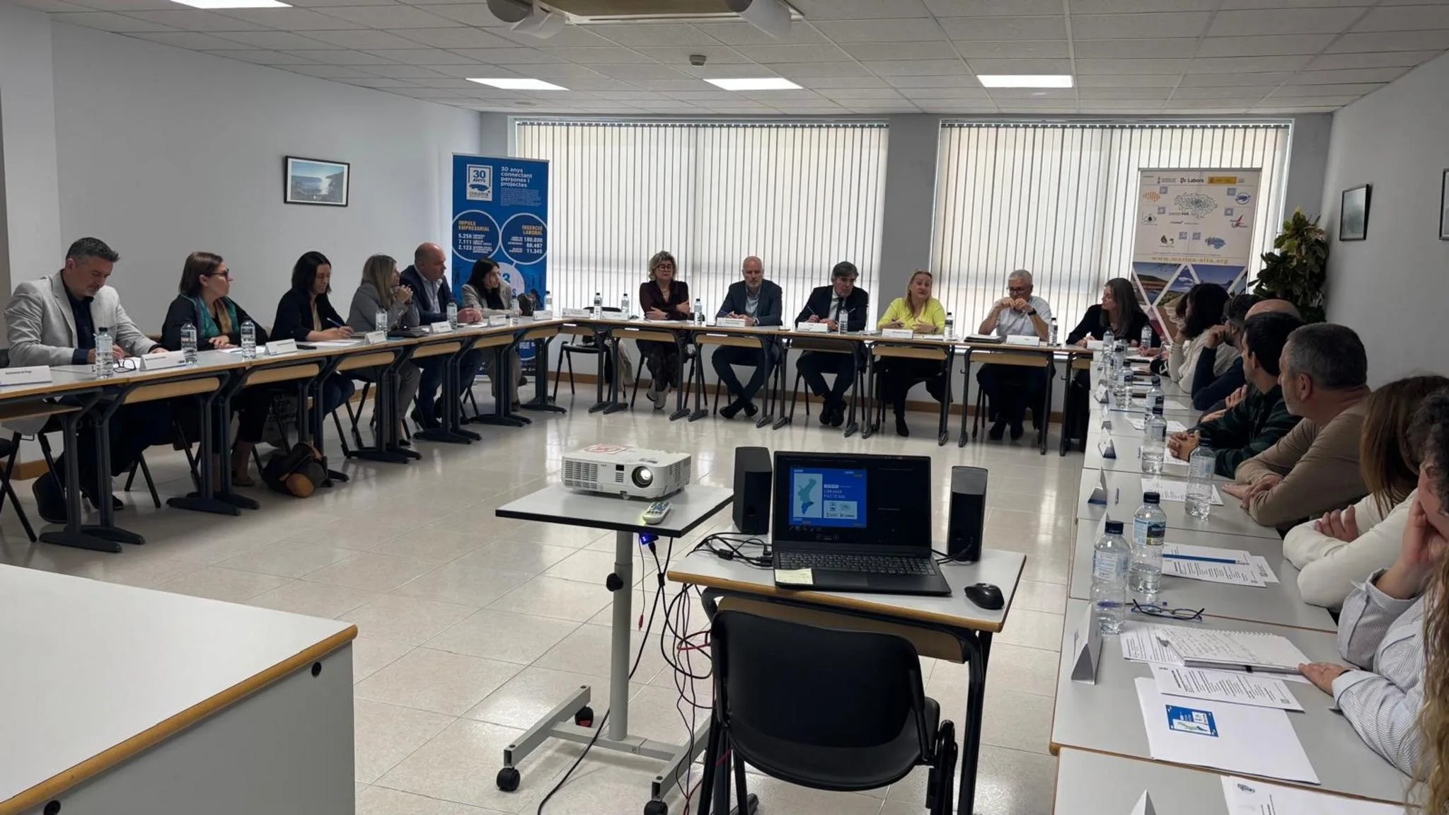 Amplia reunión de trabajo con múltiples asistentes sentados en mesas en forma de U durante la visita institucional de Labora a la sede de Creama en Dénia.