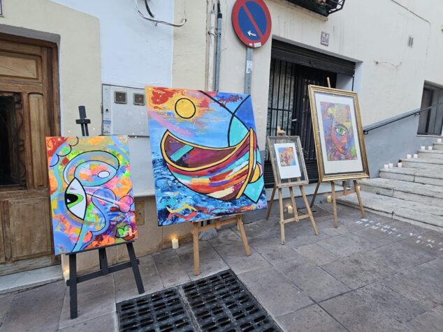 Imagen: Exposición de cuadros coloridos en caballetes con velas en el suelo en una calle del casco antiguo de Calp.