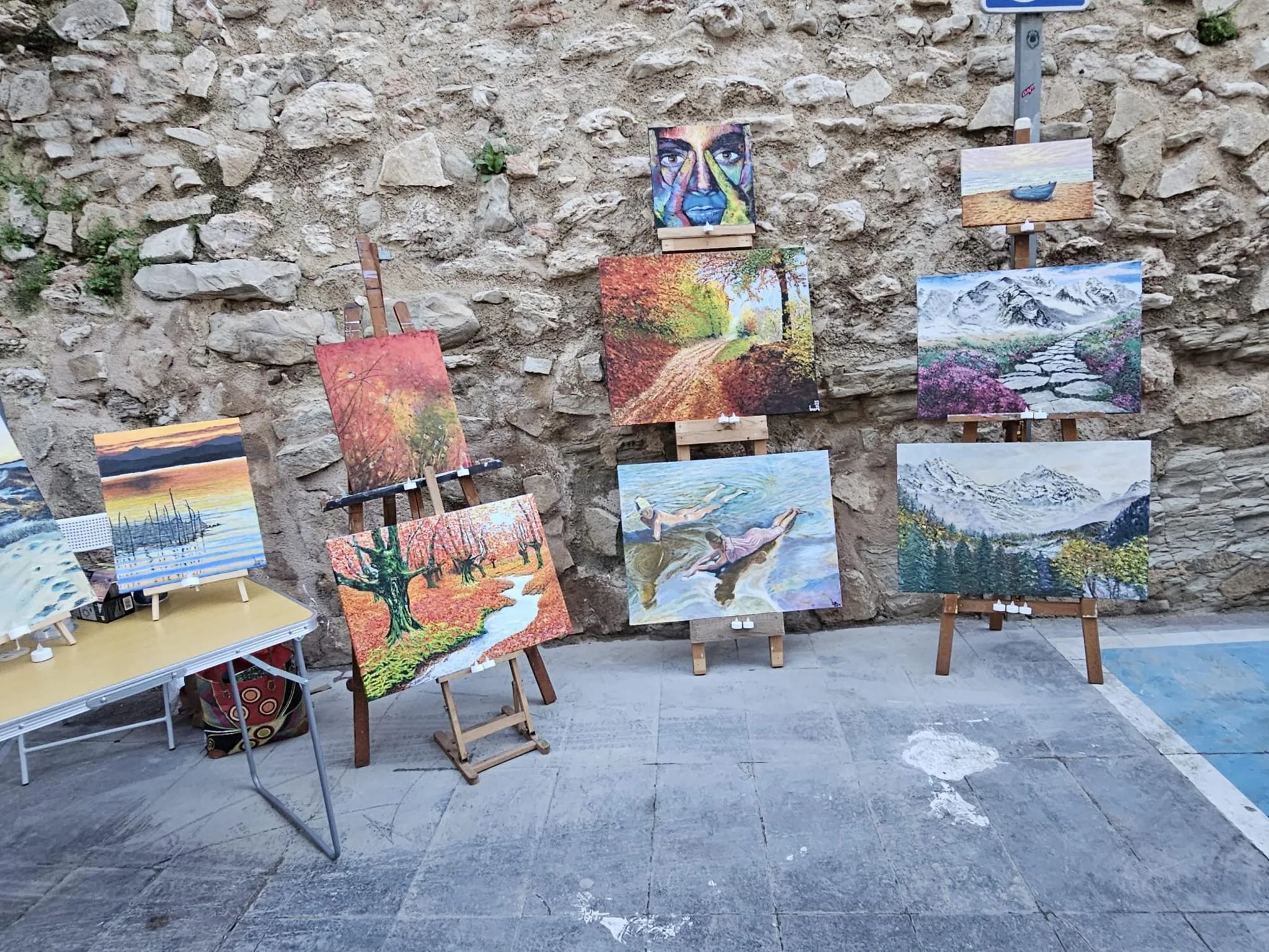 Pinturas expuestas en caballetes en una calle de piedra del casco antiguo de Calp durante el evento 'La Calle del Arte'.