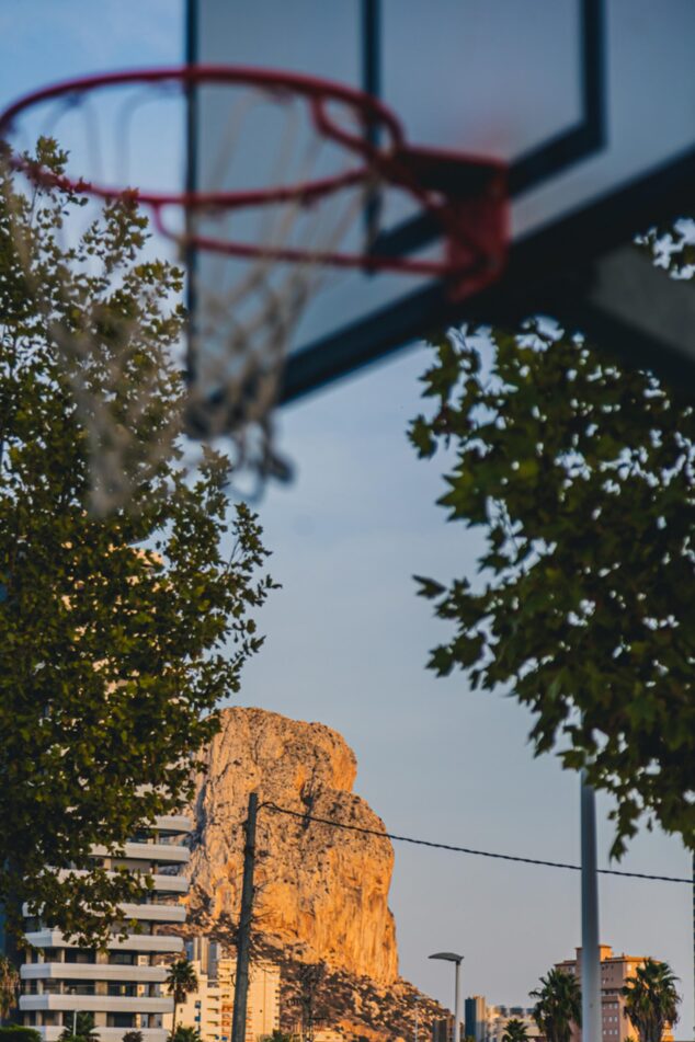 Imagen: Una canasta de baloncesto con el Peñón de Ifach y vegetación al fondo, en Calp.