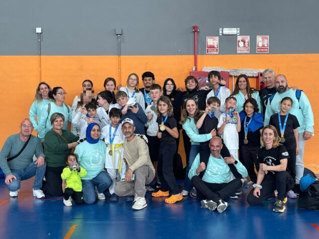 Imagen: Grupo numeroso de niños y adultos del Club de Taekwondo Athenea, muchos con medallas, posando en un gimnasio.