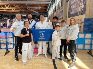 Integrantes del Club de Taekwondo Athenea de Calp posan en grupo con una bandera y medallas en un pabellón deportivo.