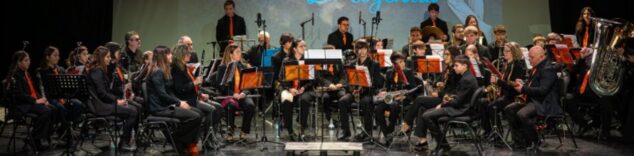 Imagen: Vista general de la Agrupació Musical CLAUdeFA–CALP actuando en un escenario, con músicos y director.