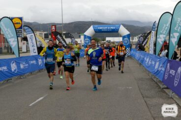 Grupo de corredores cruzando el arco de meta azul del Circuit a Peu Marina Alta durante una carrera popular.