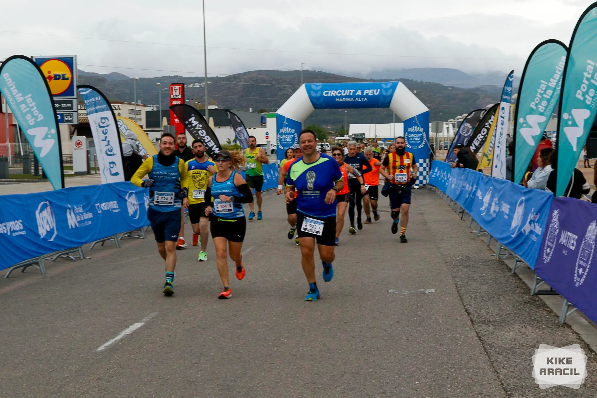 Grupo de corredores cruzando el arco de meta azul del Circuit a Peu Marina Alta durante una carrera popular.
