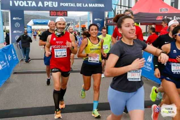 Imagen: Varios corredores participan en la carrera Volta a Peu Portal de la Marina pasando bajo el arco de meta.