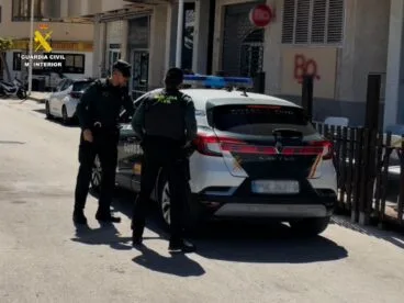 Dos agentes de la Guardia Civil junto a un coche patrulla introduciendo a un hombre detenido en la parte trasera.