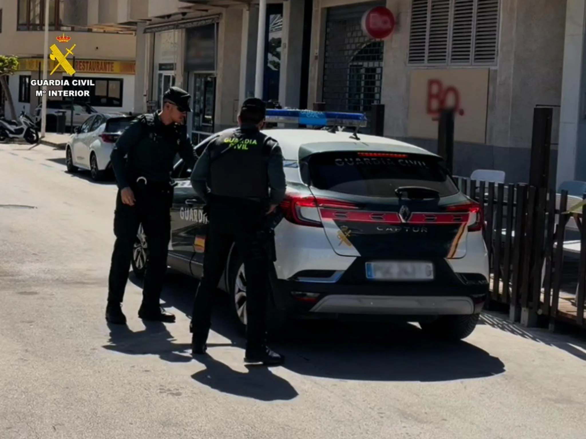 Dos agentes de la Guardia Civil junto a un coche patrulla introduciendo a un hombre detenido en la parte trasera.