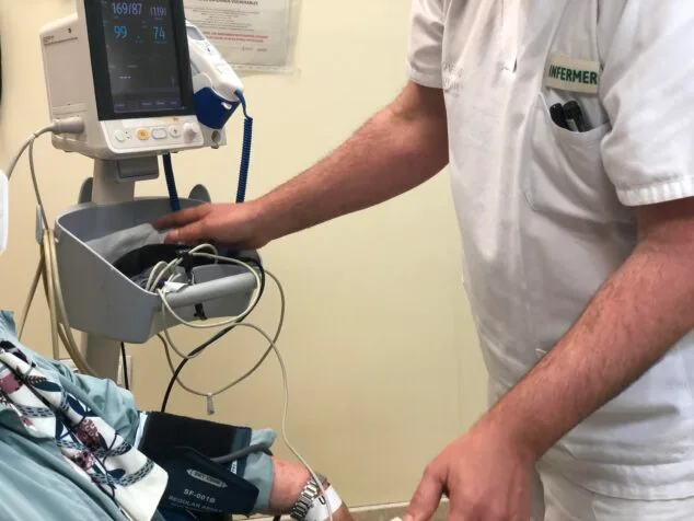 Sanitat reforça l'atenció en departaments de salut turístics aquesta Setmana Santa i Pasqua 1 Imatge: Un infermer amb uniforme blanc i el text "INFERMER" pren la pressió arterial a un pacient, el braç del qual té un maniguet connectat a un monitor de signes vitals.