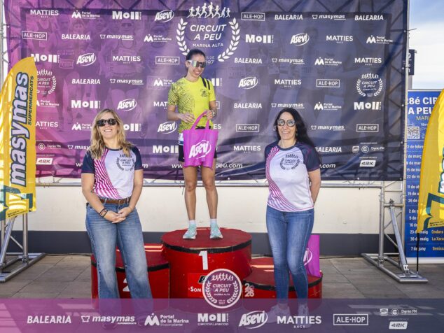 Una mujer en el primer cajón del podio sostiene una bolsa rosa de Asevi acompañada por dos mujeres.