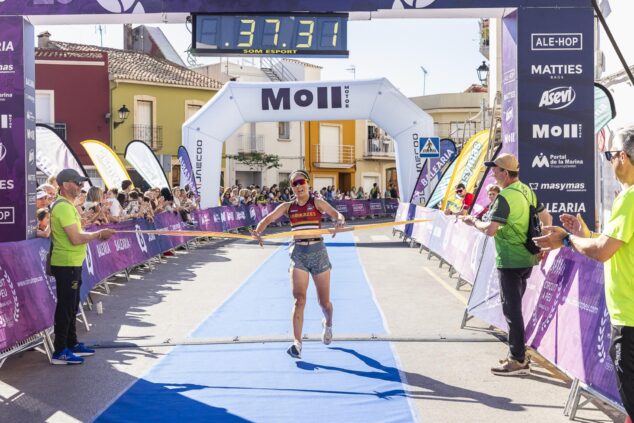 La corredora Eri Yonamine cruza la línea de meta sonriendo y rompiendo la cinta tras ganar la XVIII Volta a Peu El Verger. El reloj de meta marca 00:37:31.