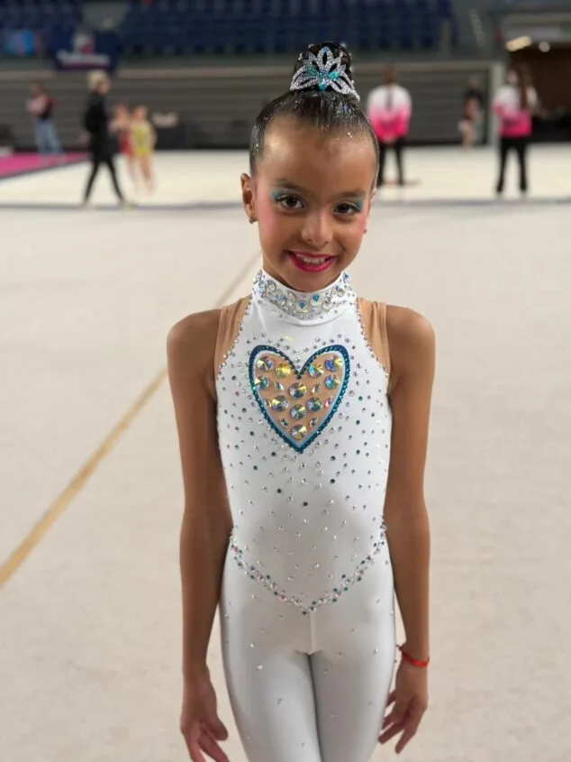 Yulen Rubio, la promesa de Calp que conquista España en gimnasia 4 Imagen: Joven gimnasta del Club Les Marines posa sonriente con un maillot blanco decorado con brillantes en el pabellón de competición.
