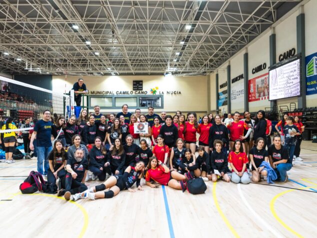Imagen: Foto de grupo numeroso de jóvenes jugadoras de voleibol, entrenadores y organizadores en una cancha polideportiva cubierta en La Nucía.