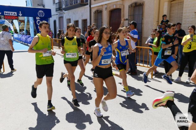 Imagen: Varios corredores jóvenes con dorsales compiten intensamente en una carrera urbana.