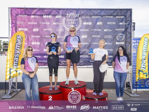 Cinco mujeres atletas en un podio con trofeos y bolsas de regalo delante de una pancarta del Circuit a Peu Marina Alta.