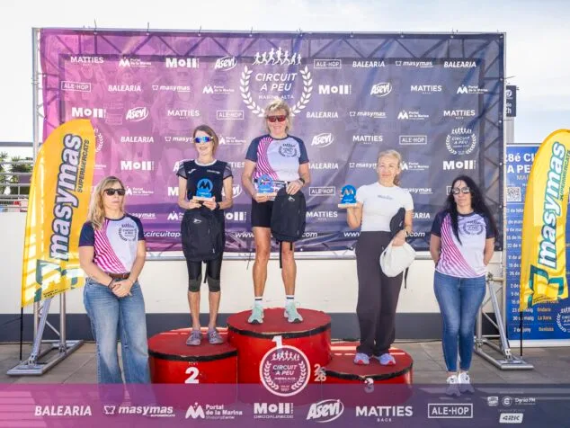 Cinco mujeres atletas en un podio con trofeos y bolsas de regalo delante de una pancarta del Circuit a Peu Marina Alta.
