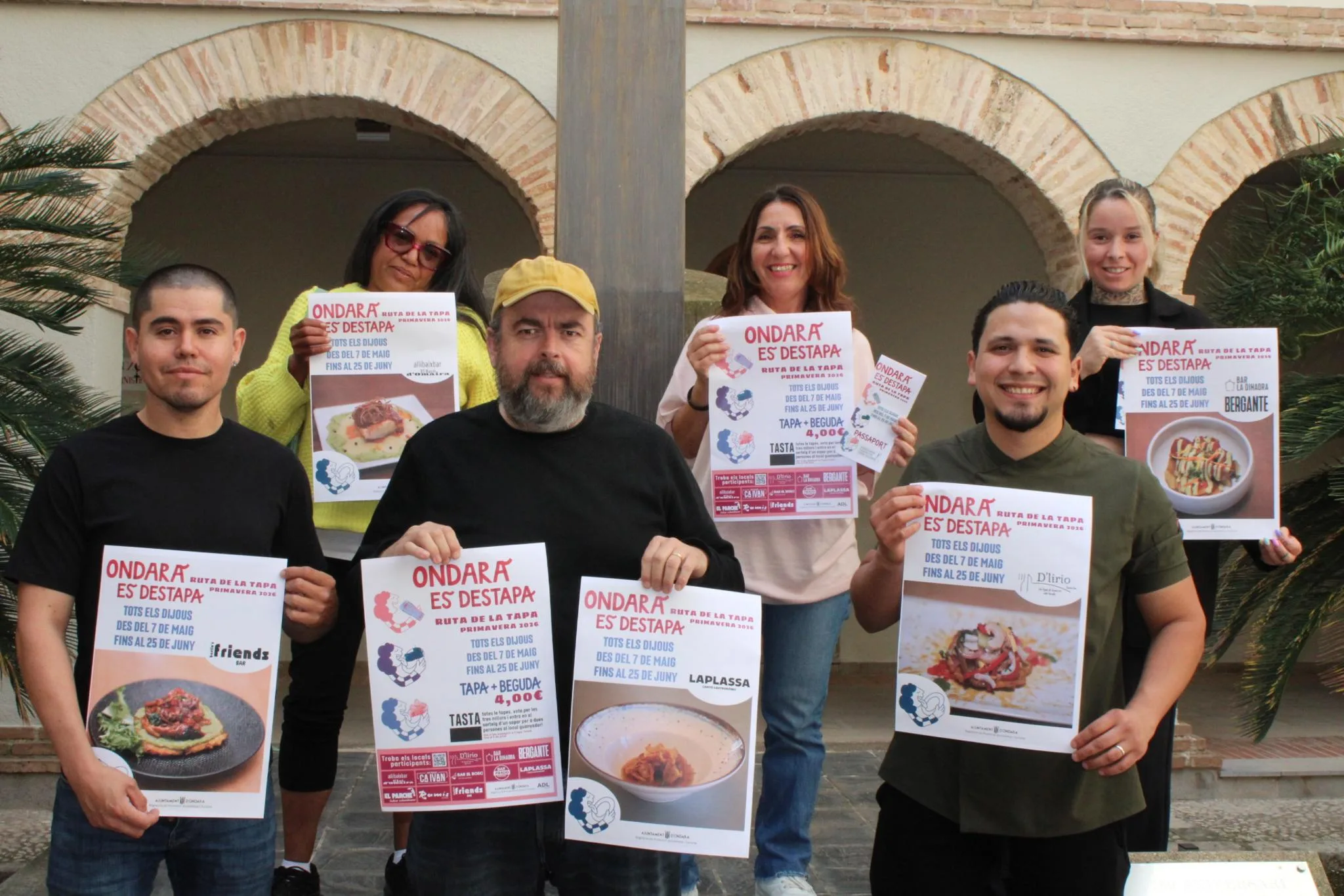 Grupo de seis restauradores sosteniendo carteles promocionales de la Ruta de la Tapa de Ondara Primavera 2026 en un patio.