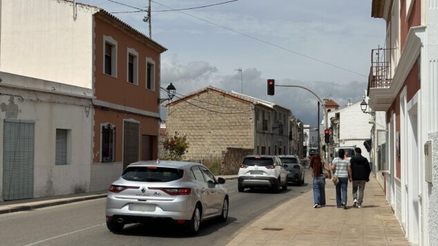 Imagen: Vista de una calle en Els Poblets con coches parados en un semáforo en rojo y personas caminando por la acera.