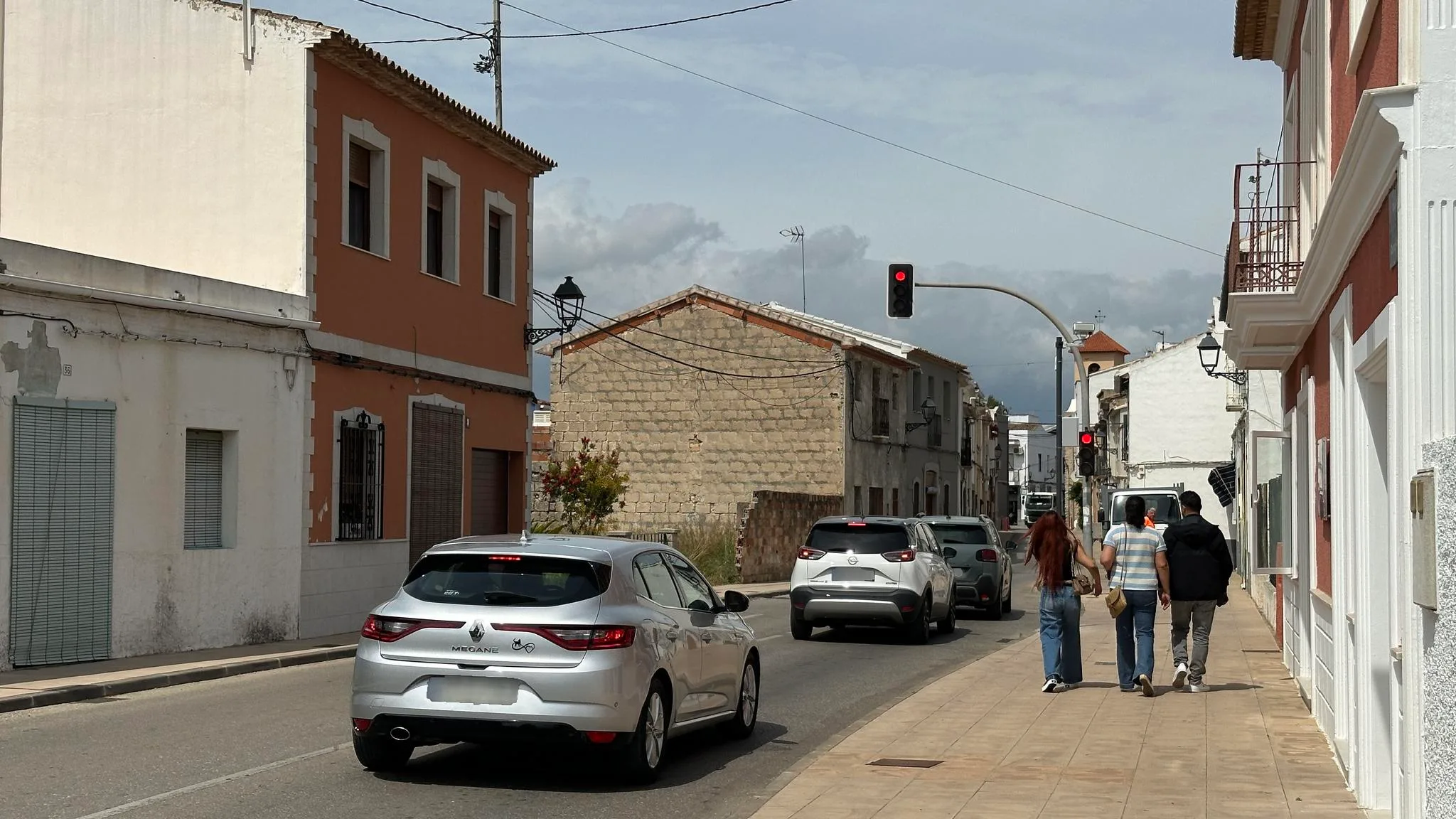Vista de una calle en Els Poblets con coches parados en un semáforo en rojo y personas caminando por la acera.
