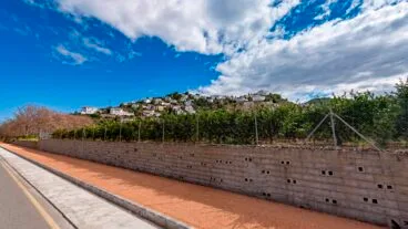 Vista exterior de la urbanización Monte Pego, con casas blancas escalonadas en una colina bajo un cielo con nubes.