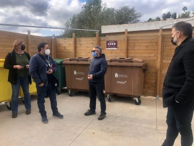 Imagen: Varias personas de pie junto a contenedores marrones de basura orgánica con los logotipos del Ajuntament de Pedreguer y Fovasa.