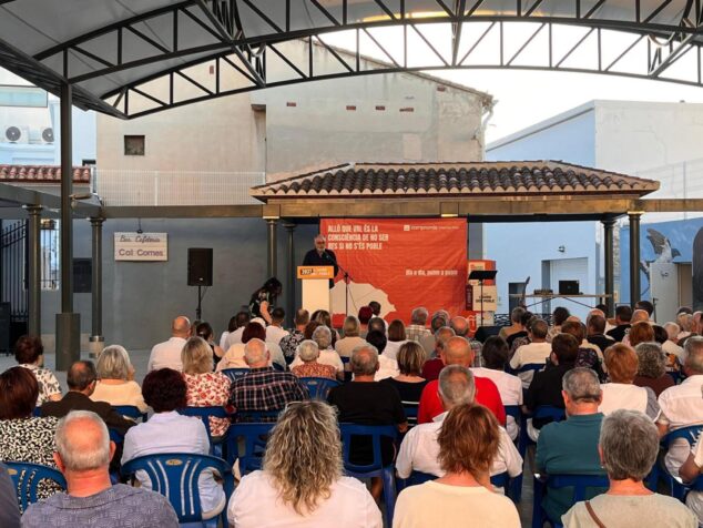 Compromís conmemora 15 años en la alcaldía de Pedreguer y activa su precampaña para 2027 2 Imagen: El alcalde Sergi Ferrús habla desde un atril en un escenario al aire libre durante el acto de Compromís en Pedreguer ante el público sentado.