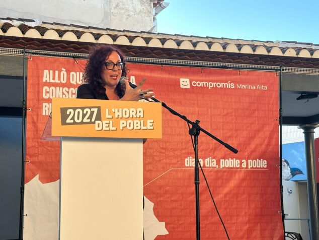 Compromís conmemora 15 años en la alcaldía de Pedreguer y activa su precampaña para 2027 14 Una ponente habla en un atril con el lema "2027 L'HORA DEL POBLE" durante un acto de Compromís Marina Alta.