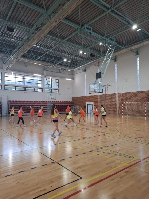 Grup de joves jugadores jugant un partit de bàsquet en un pavelló esportiu interior.