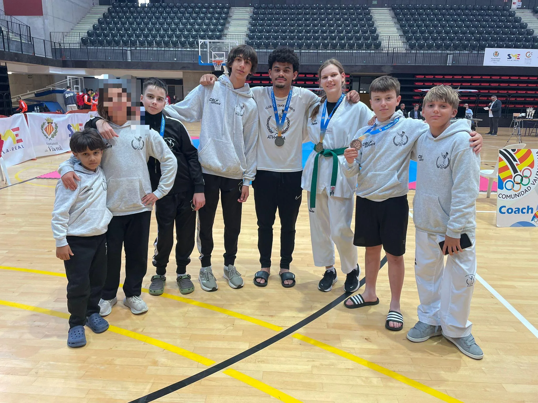 Foto de grupo de ocho miembros del Club Taekwondo Athenea, incluyendo deportistas con medallas y entrenadores, en el pabellón de Villarreal.