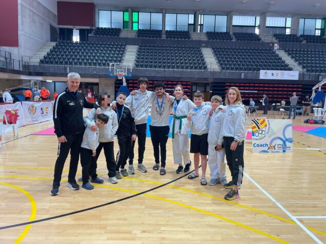 Imagen: Grupo de nueve jóvenes taekwondokas, algunos con medallas, y sus dos entrenadores del Club Athenea posando en una pista deportiva cubierta.