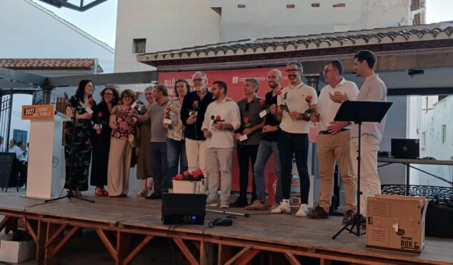 Compromís conmemora 15 años en la alcaldía de Pedreguer y activa su precampaña para 2027 6 Imagen: Grupo de representantes de Compromís sosteniendo rosas en un escenario al aire libre durante el acto político en Pedreguer, con un atril que dice '2027 L'HORA DEL POBLE'.