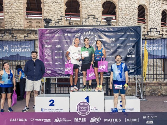 Corredores premiados en el podio de la Cursa Popular de Ondara sosteniendo bolsas y trofeos del patrocinador Asevi.