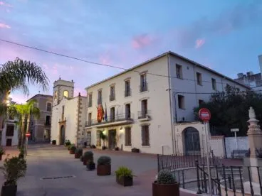 Vista exterior del edificio del Ayuntamiento de Ondara al atardecer con banderas en el balcón.