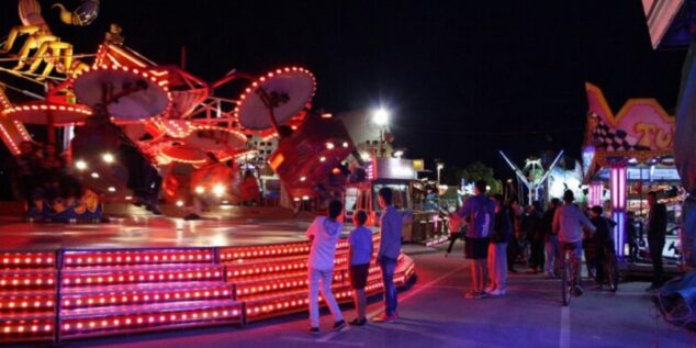 Imagen: Atracción de feria iluminada dando vueltas por la noche con gente mirando.