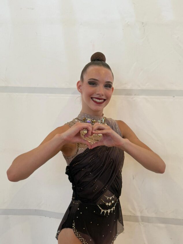 Imagen: Una gimnasta del C.G. Les Marines sonríe y hace un corazón con las manos con el maillot de competición.