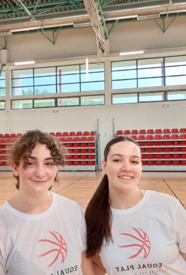 Imagen: Dos jóvenes jugadoras de baloncesto sonríen a cámara en un pabellón deportivo, vistiendo camisetas blancas con el logo del proyecto EQUALPLAY.