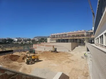 El nuevo IES Les Salines de Calp fija su apertura para enero de 2027 9 Vista de una obra en construcción con maquinaria y un edificio con andamios bajo un cielo azul.