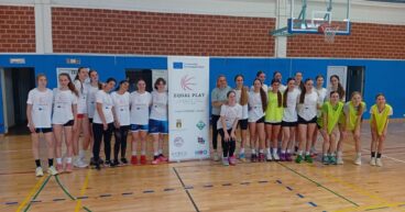 Foto de grupo de jóvenes jugadoras de baloncesto y entrenadores en un gimnasio, posando junto a un cartel del proyecto europeo EQUAL PLAY.