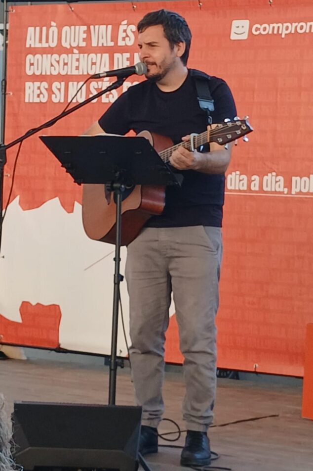 Compromís conmemora 15 años en la alcaldía de Pedreguer y activa su precampaña para 2027 5 Imagen: El cantautor Pau Alabajos toca la guitarra y canta en un escenario con un fondo naranja de Compromís.