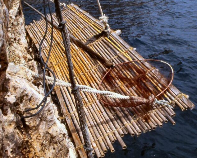 Primer plano de una antigua estructura de pesca ('pesquera') construida con cañas, cuerdas y madera en la pared de un acantilado sobre el mar.